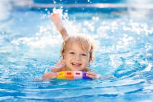 A child floats and splashes in an above ground pool with a huge smile on her face.