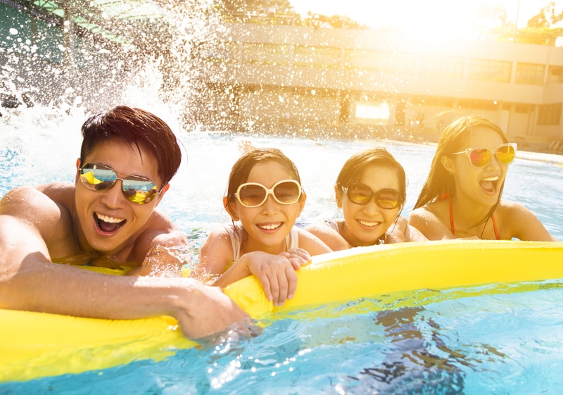 A family of four splashes in a pool while holding onto a yellow pool float. They optimized their pool budget.