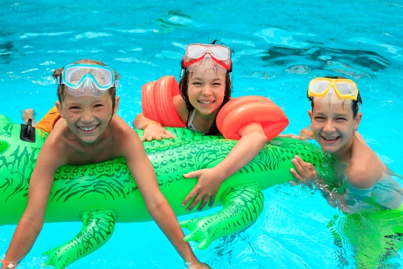 A group of children play in a swimming pool with a green alligator float. They are enjoying the benefits of fiberglass swimming pools.
