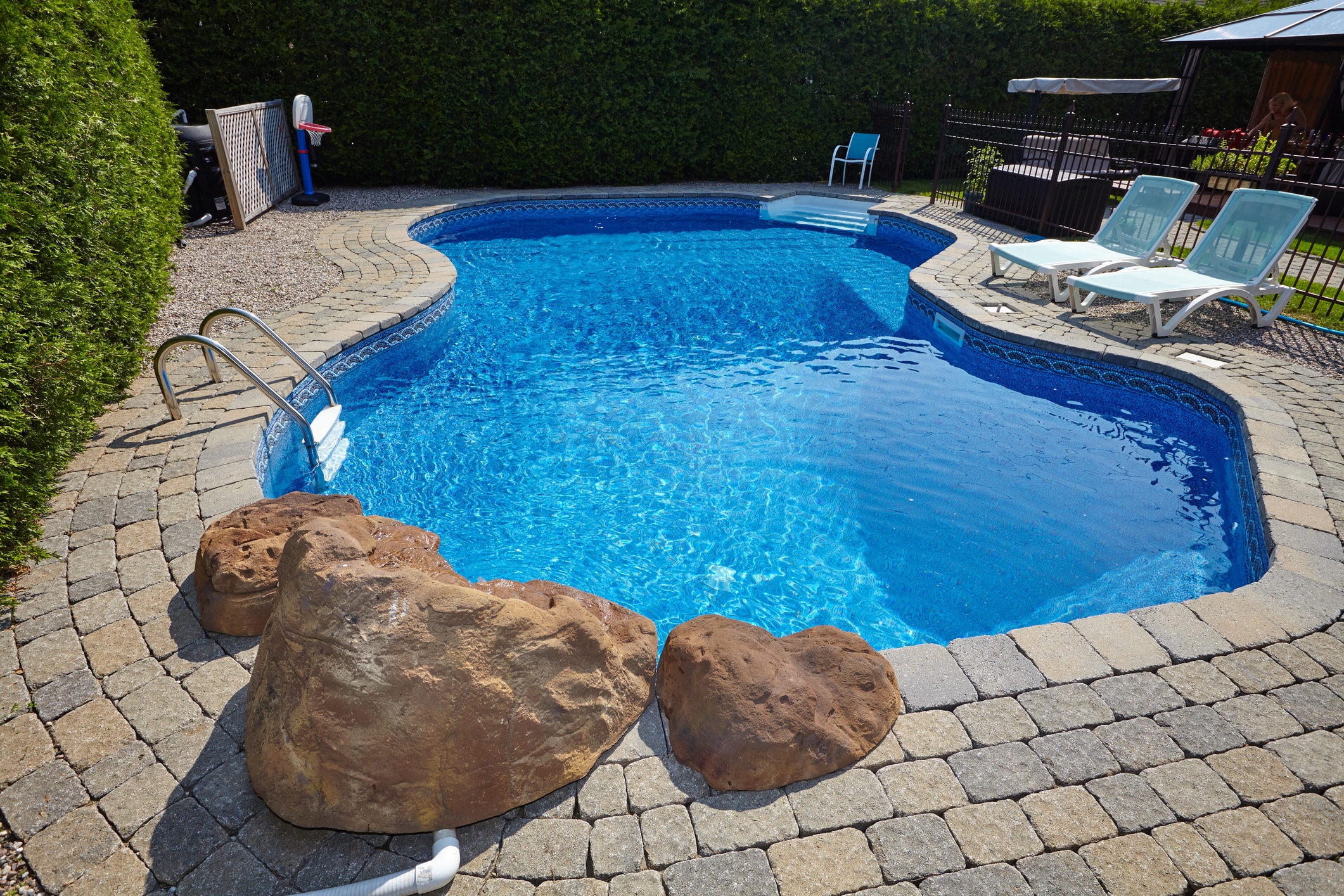 a swimming pool with hardscaping and lounge chairs.