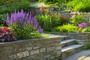 an updated backyard design and landscaping with rock wall, steps, and colorful flowers