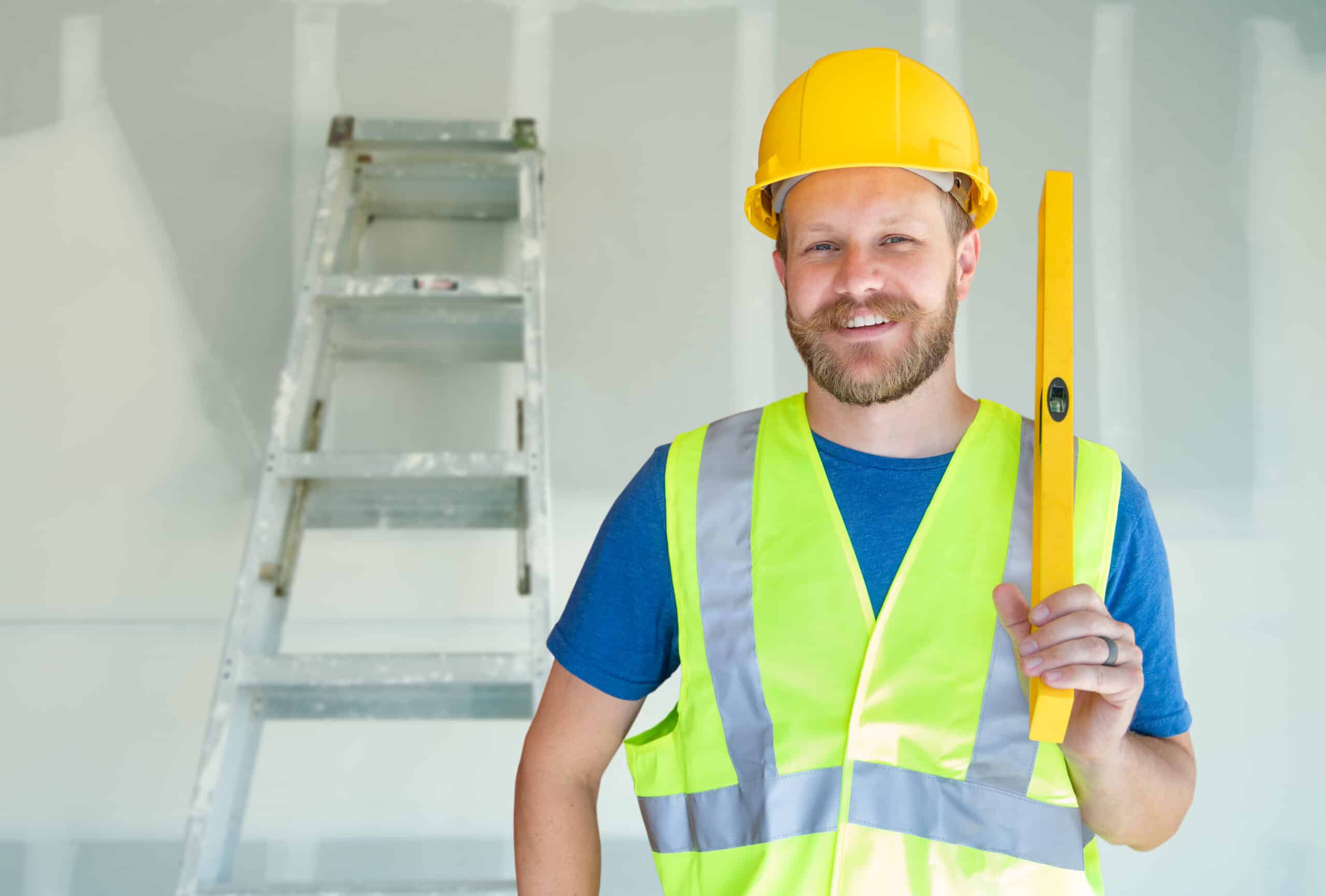 Your competitors are tough when you're a home improvement contractor. This contractor is considering all the ways to edge out the competition while wearing a bright safety vest, yellow hard hat, and holding a yellow level.