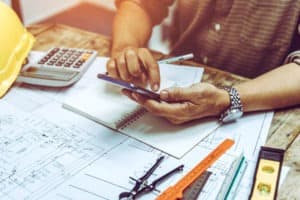 Grow your contracting business by putting in the hard work. A contractor sits with paperwork and a calculator to figure out how.