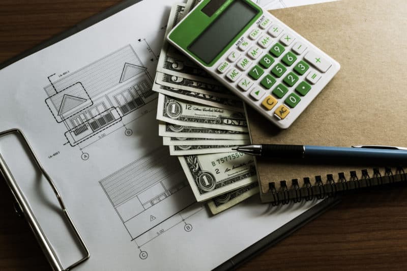 a notebook, calculator, and money on top of contracting blueprints