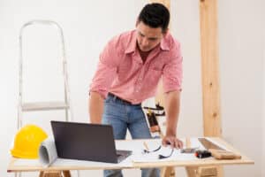 A dark haired general contractor is working on his laptop with his tools around him. He's building a website that has everything a general contractor should have in a website.