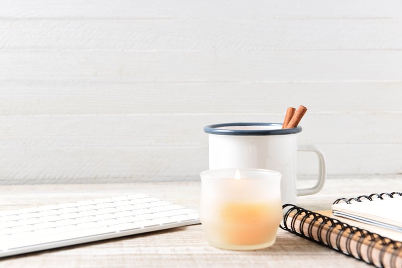 A coffee mug and scented candle sit on an office desk. Engaging your senses is one of our 3 practical anti-stress tips for business owners.