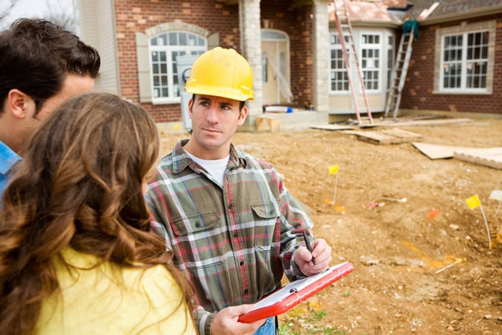 general contractor meets with clients in front of house construction 