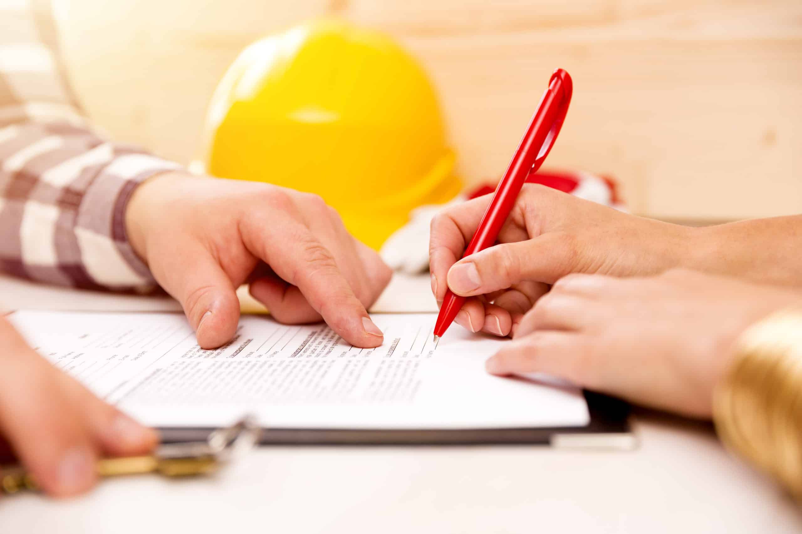 We see the hands of a contractor who offers financing points to the contract as his client signs it. A hard hat is in the background.