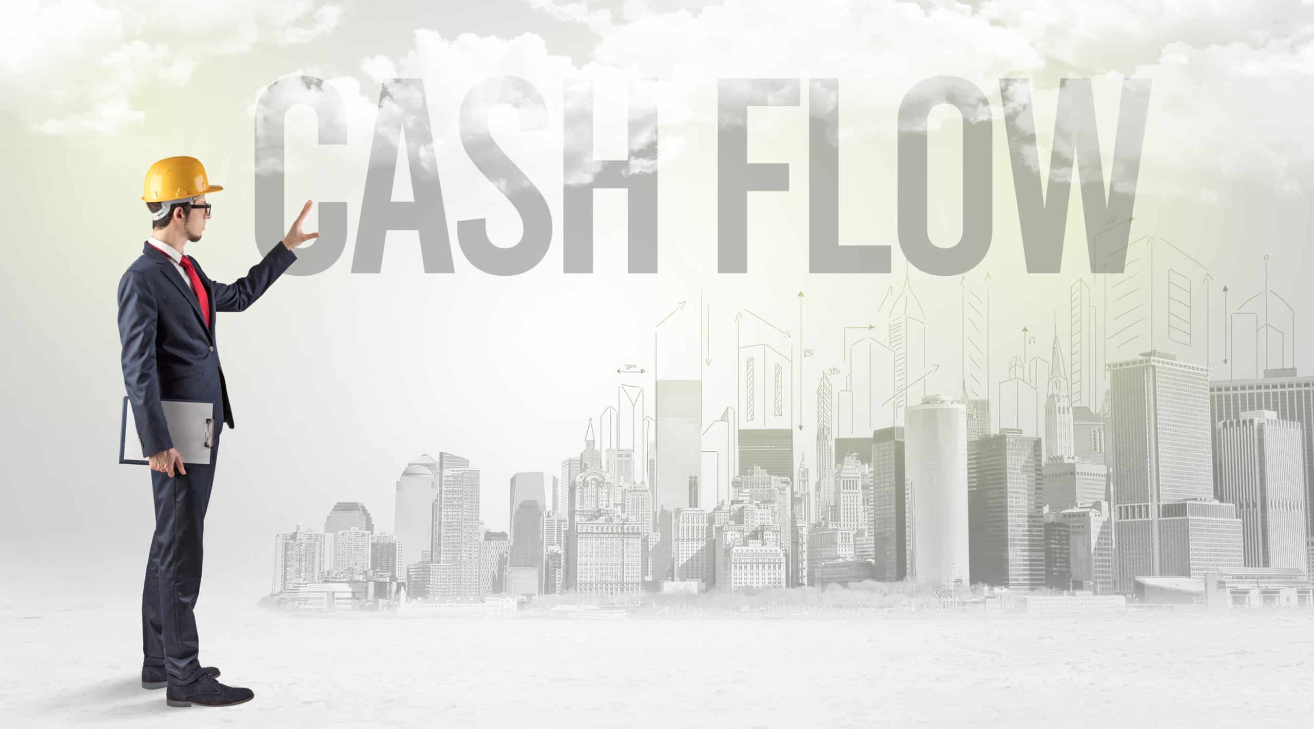 a man dressed in a suit and hard hat contemplates solving his cash flow issues while he points to the words "cash flow" in the background
