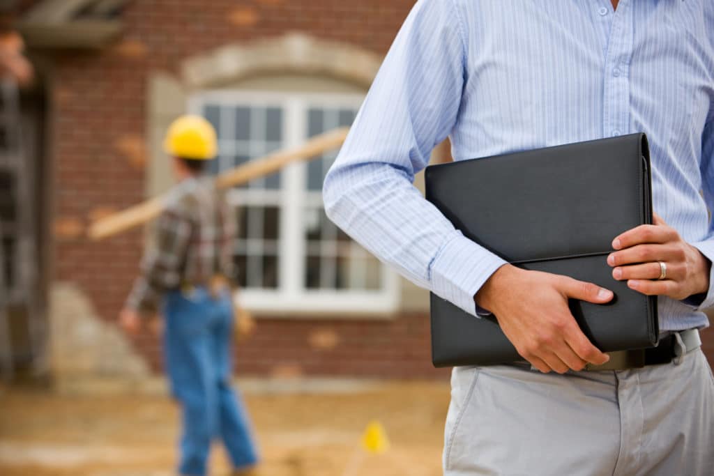 a man holds a portfolio while another contractor walks across the worksite in the background