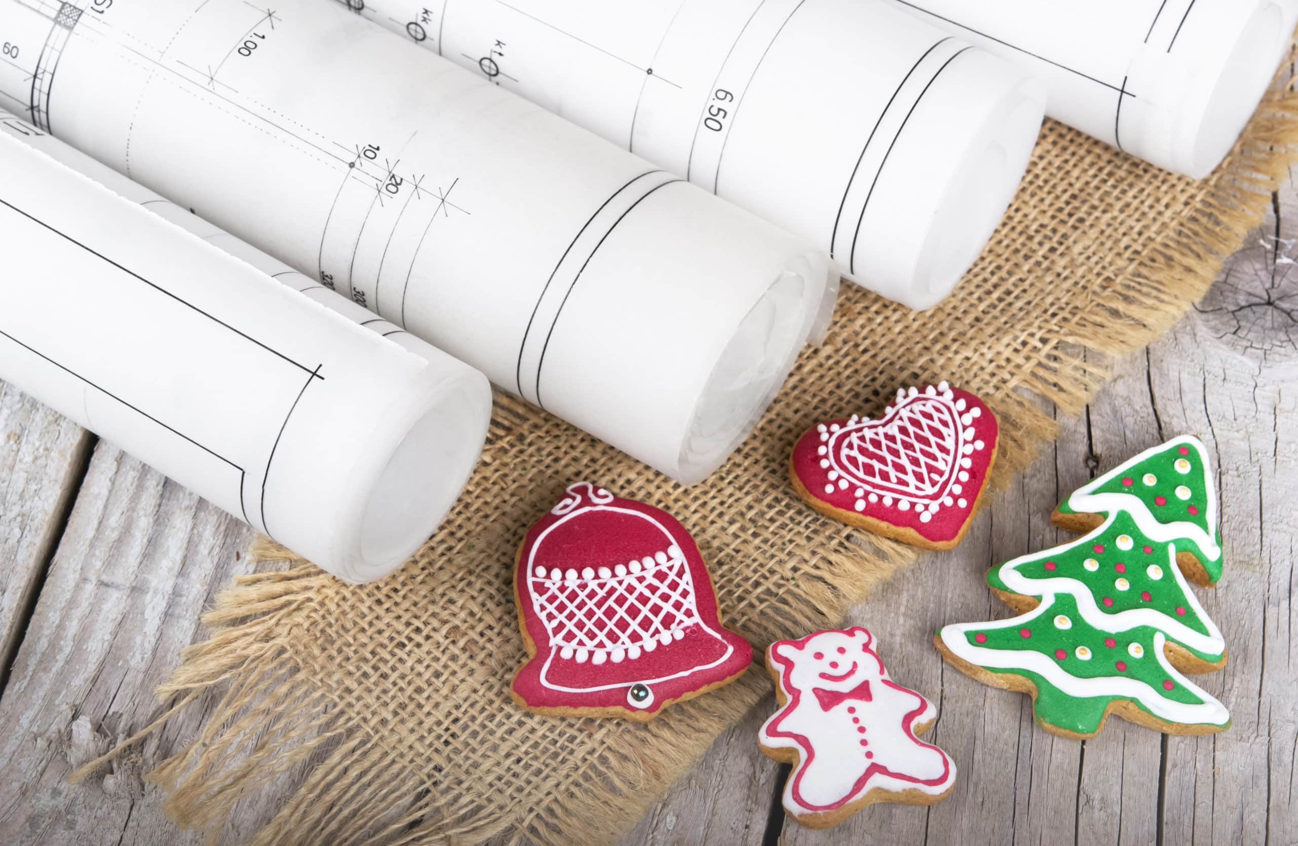 rolled blue prints sit on top of a table next to some holiday cookies as contractors contemplate holiday social media posts
