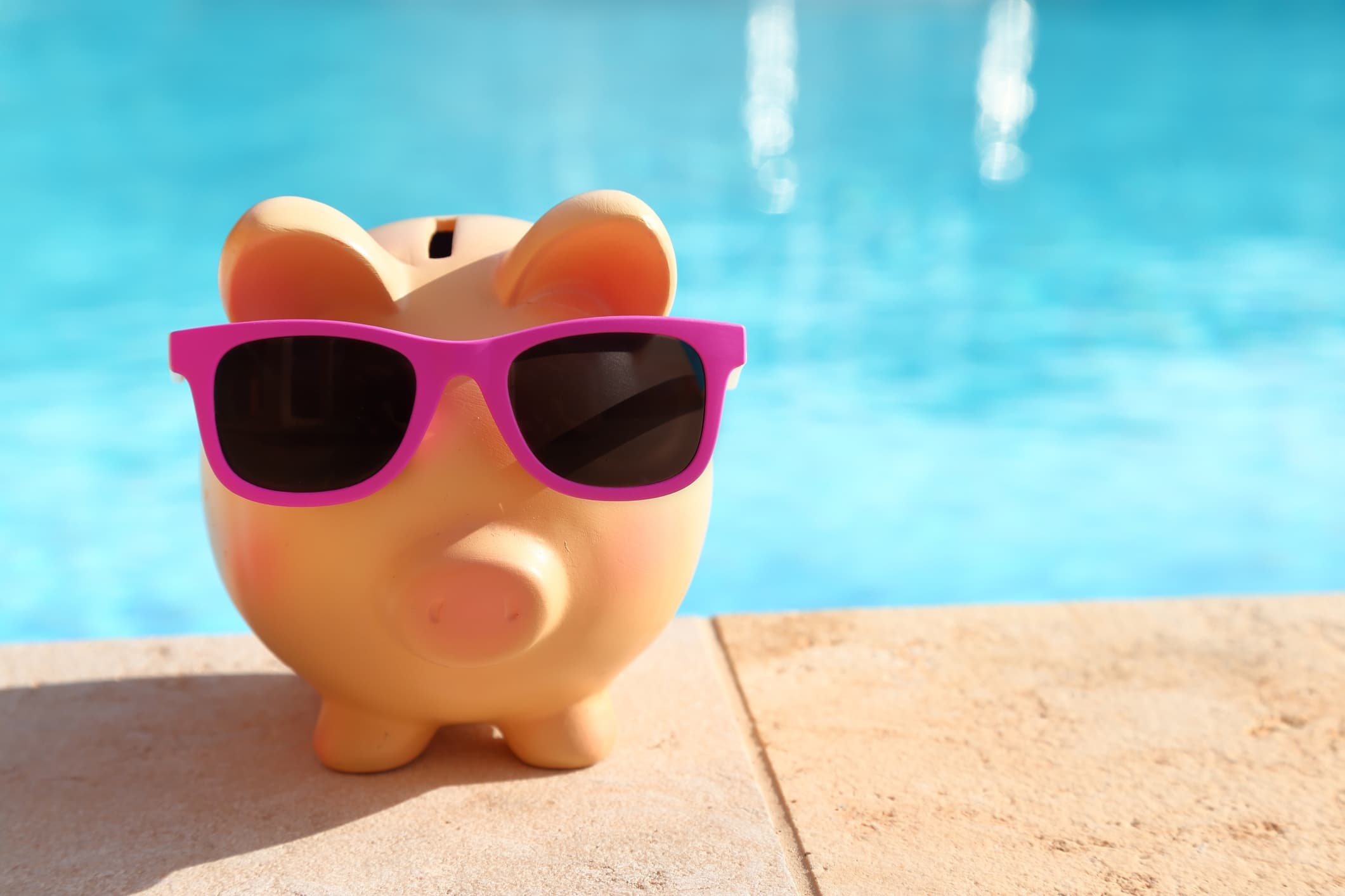 Piggy banks with sunglasses in front of swimming pool