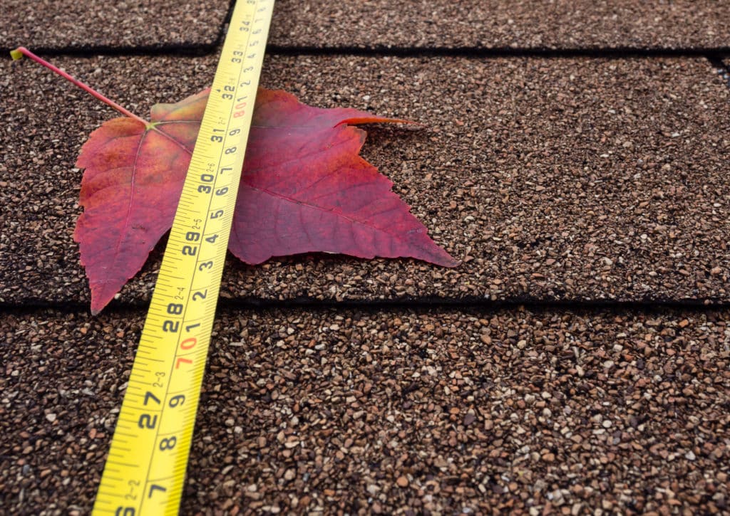 a red leaf sits atop a roof with a measuring tape stretched over it