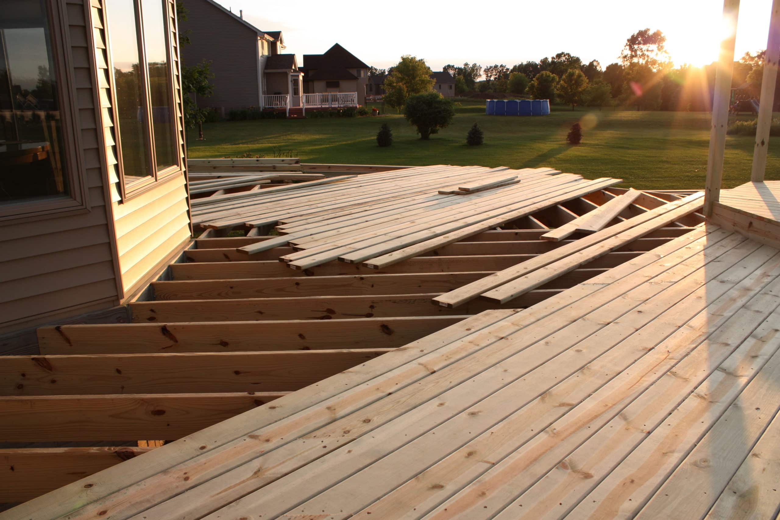 Cut lumber sits on top of a partially built deck with a beautiful sunset in the background since the deck and patio business builders have finished for the day.