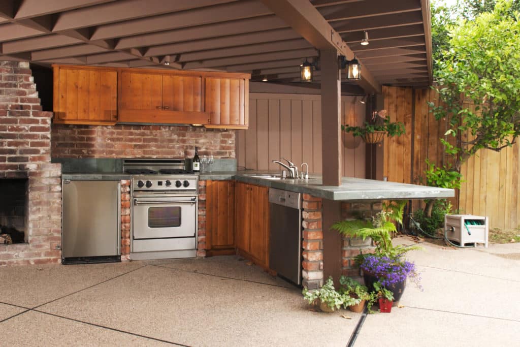 An outdoor kitchen with wooden cabinets and brick backsplash was installed by a door and window business. 