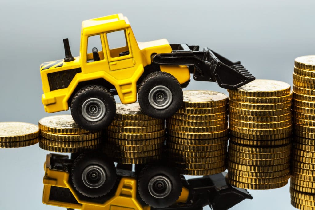 A tiny toy excavator climbs small stacks of coins. 