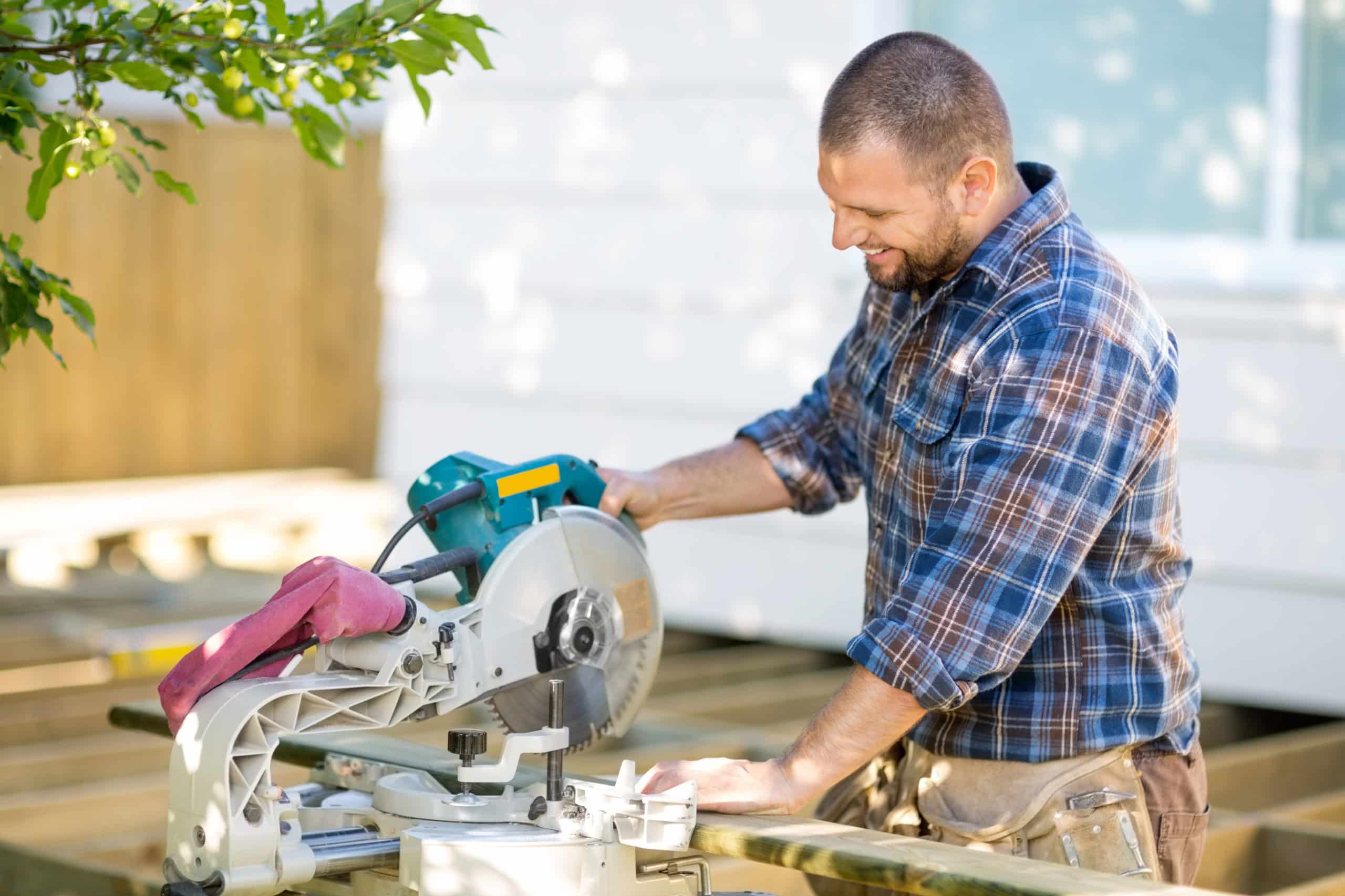 A fencing and decking business contractor uses a compound miter saw to cut boards for his latest deck build.