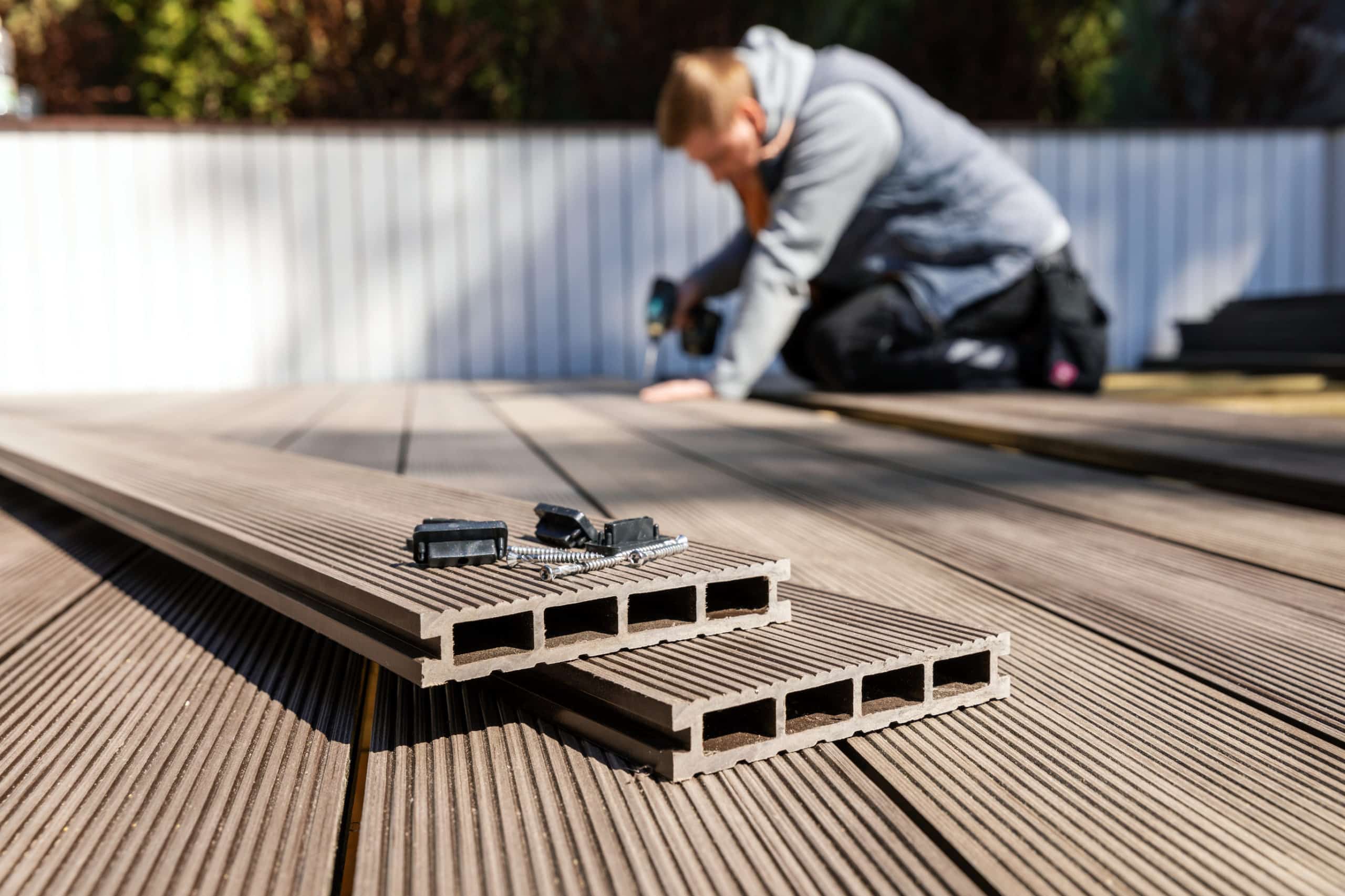 A decking and fencing contractor who is dominating the competition builds a deck from composite materials. He is in the background working while his building materials are stacked in the foreground.