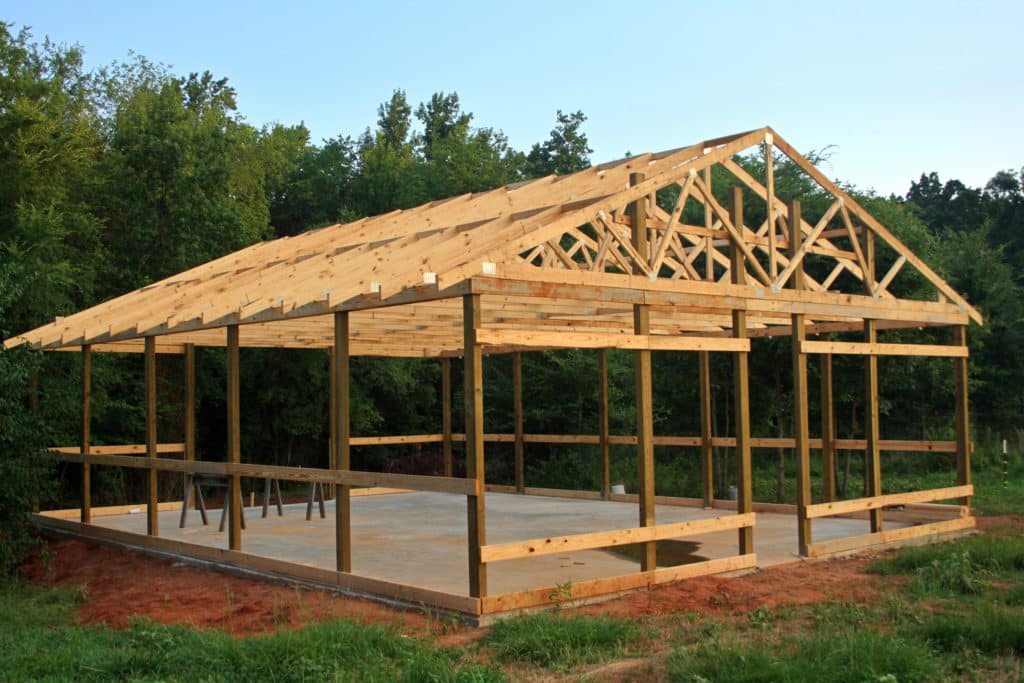 A half-constructed pole barn sits on a concrete foundation and is being built by a pole barn and steel building business.