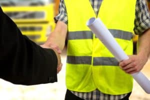 steel building contractor holds construction documents and shakes hands with client