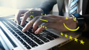 A man in a business suit types on a laptop keyboard. He learns that online reviews are important as a series of smiley faces and frowning faces appear above his hands with corresponding starred ratings.