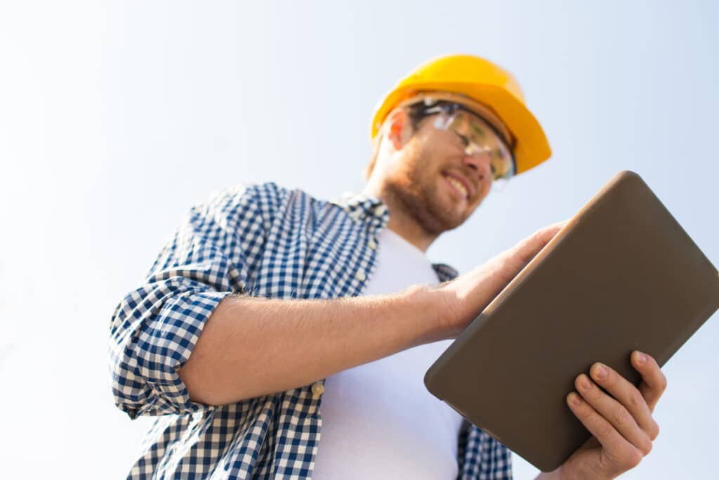 A home improvement contractor is looking at his tablet device while wearing a hard hat. He wants to dominate the competition in your market. 