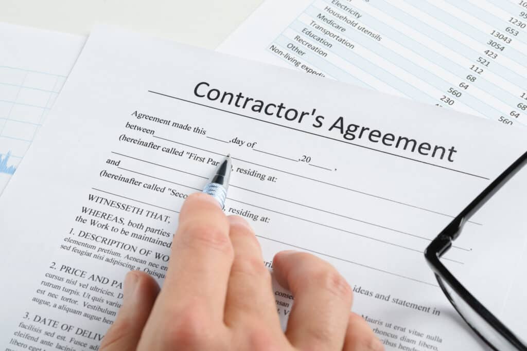 A man's hand holds a pencil and looks at a contractor's agreement. 