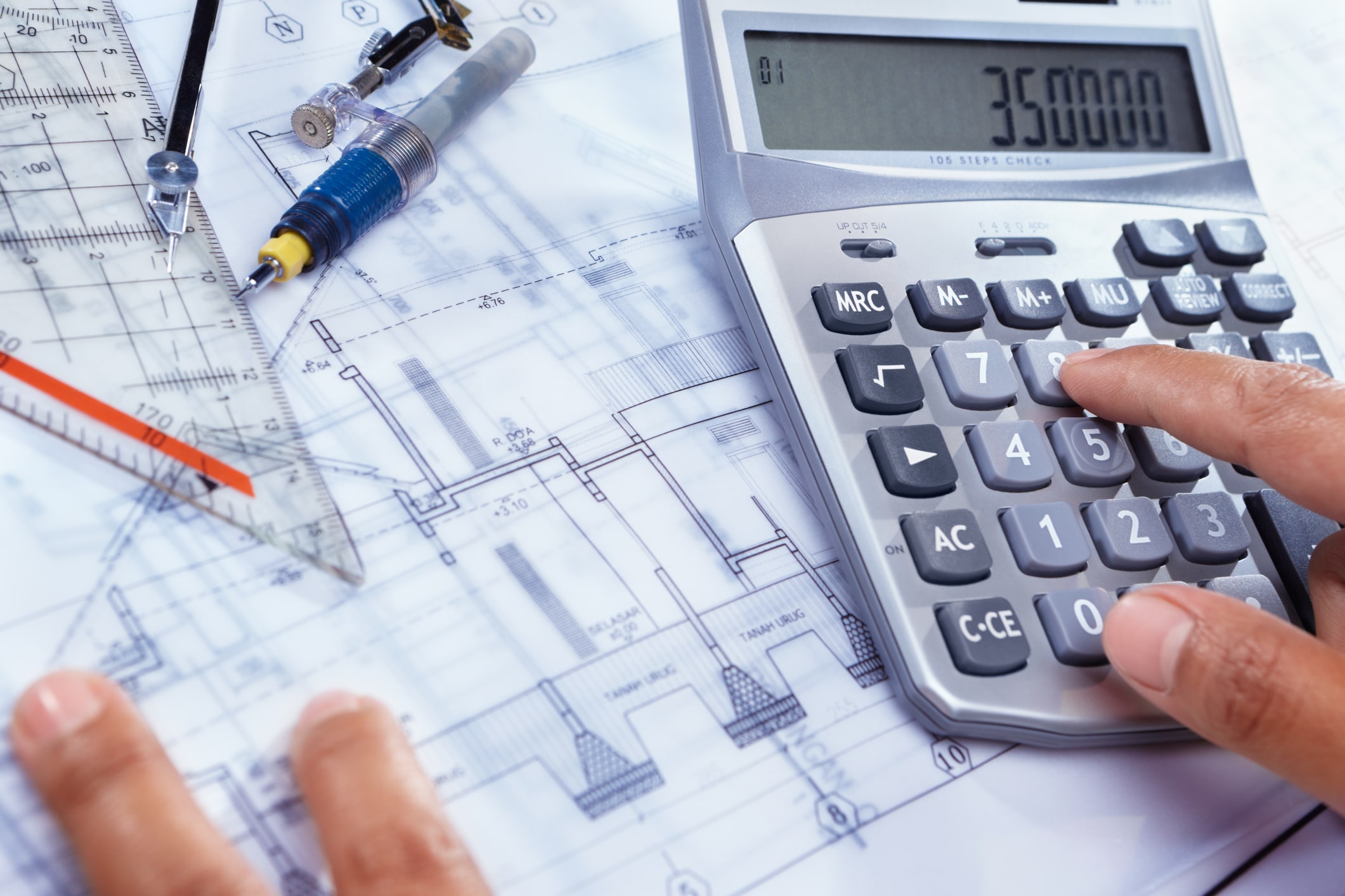A contractor uses a calculator to estimate builder loans and general contractor financing over project blueprints